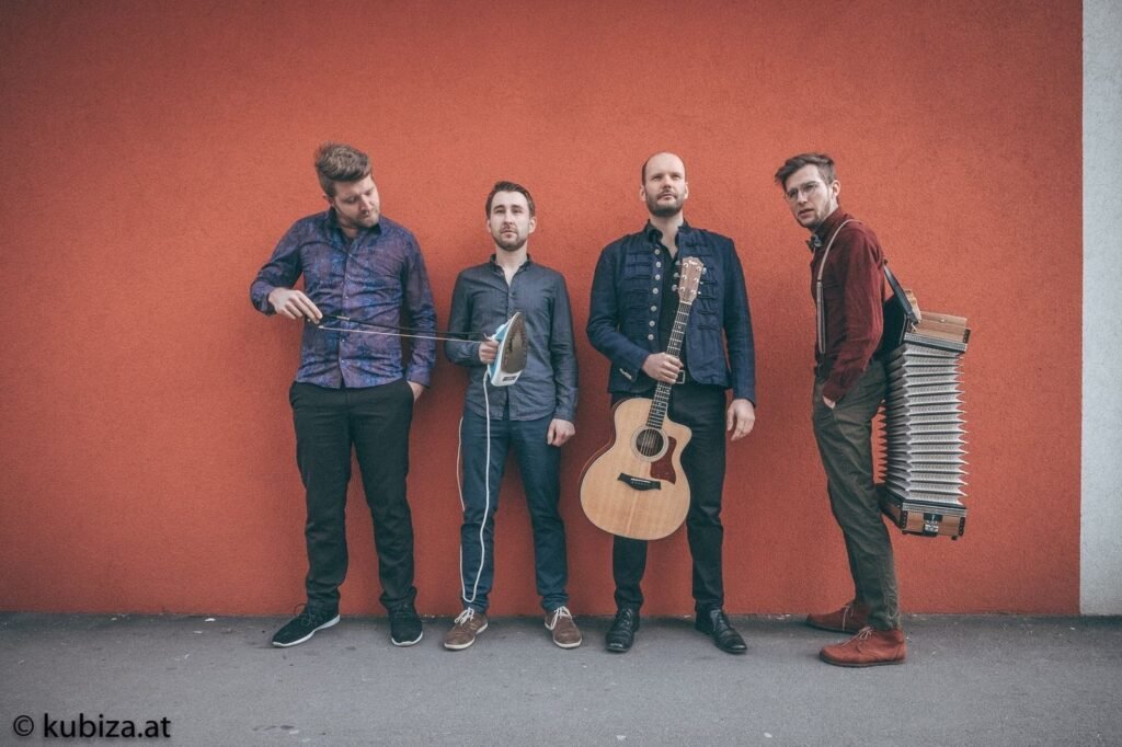 Bandfoto Mamabeda vor roter Wand mit Gitarre und Harmonika