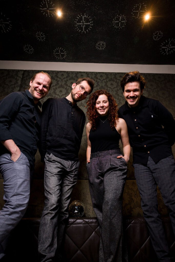 Bandfoto Annagramm 2026: vier Musikerinnen und Musiker vor dunkler Wand