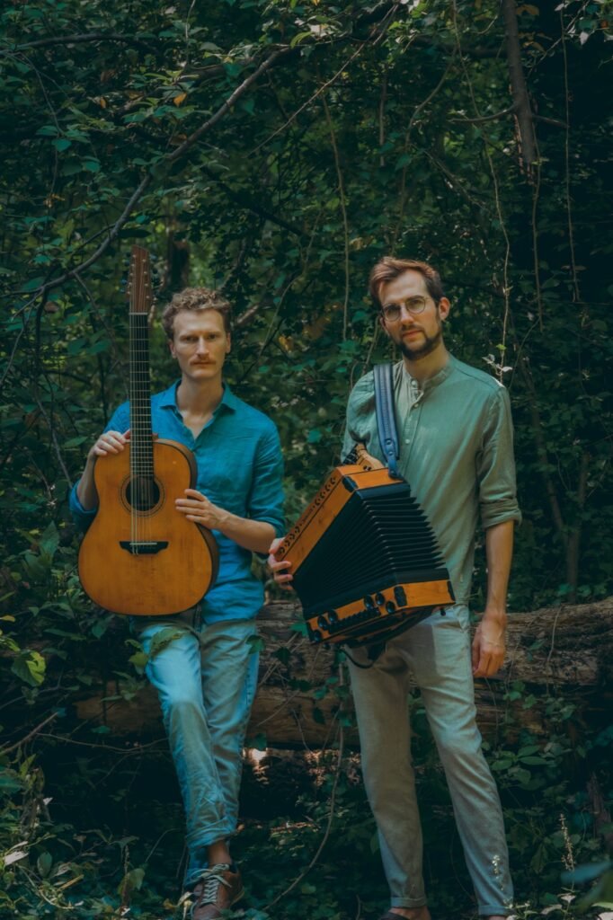 Timmy Gasslander mit Gitarre und Jonny Kölbl mit Steirischer Harmonika stehen nebeneinander im Wald