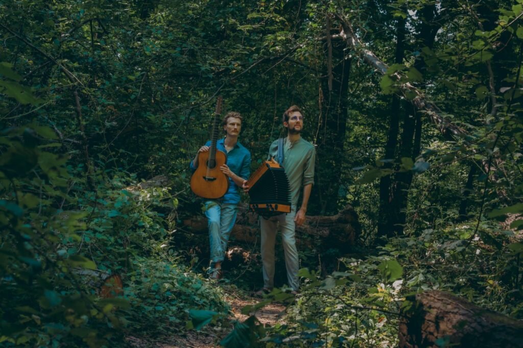 Tim & Jonnic mit Gitarre und Harmonika zwischen dichtem Grün im Wald