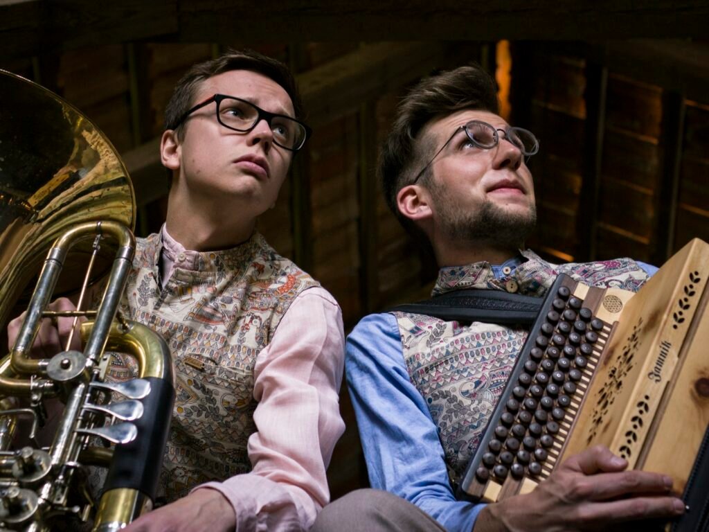 Tobias Weiß mit Tuba und Jonny Kölbl mit Steirischer Harmonika in Trachtenwesten, beide blicken nach oben